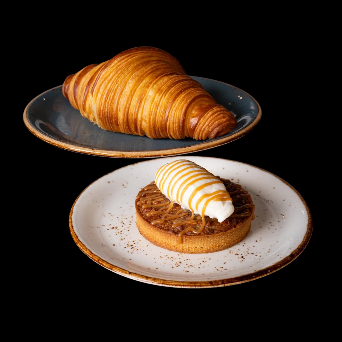 A croissant on a blue plate and a caramel-topped tart with a scoop on a white plate