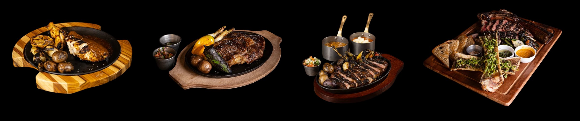 Four plates: chicken with potatoes and charred onions on a wooden board, a steak on a cast-iron plate with small cups of sauce, sliced steak with potatoes and two small copper pots, and a bone-in steak on a board with marrow bones