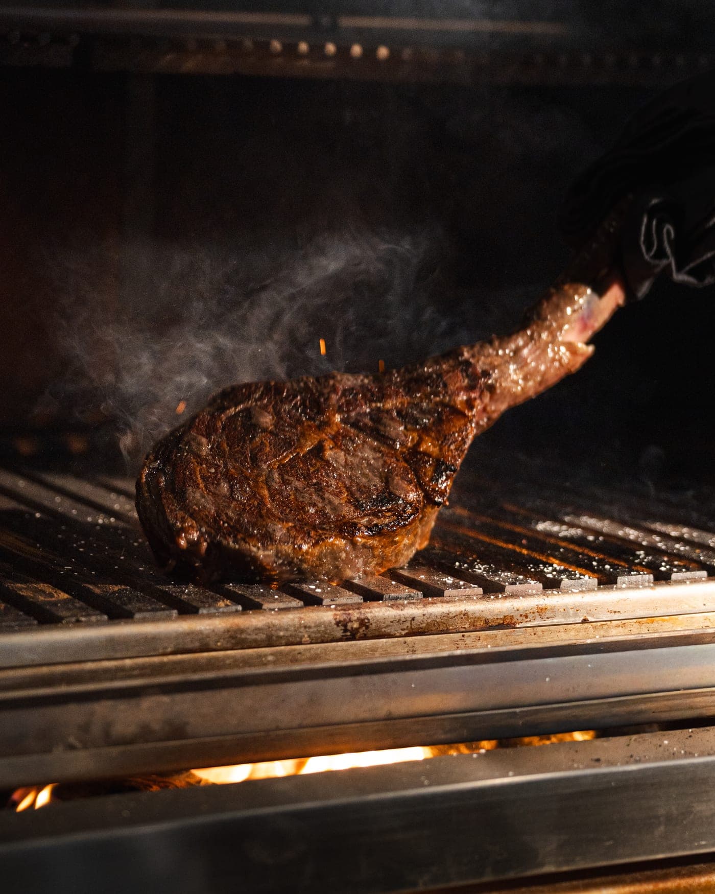 A tomahawk steak on the grill as smoke rises