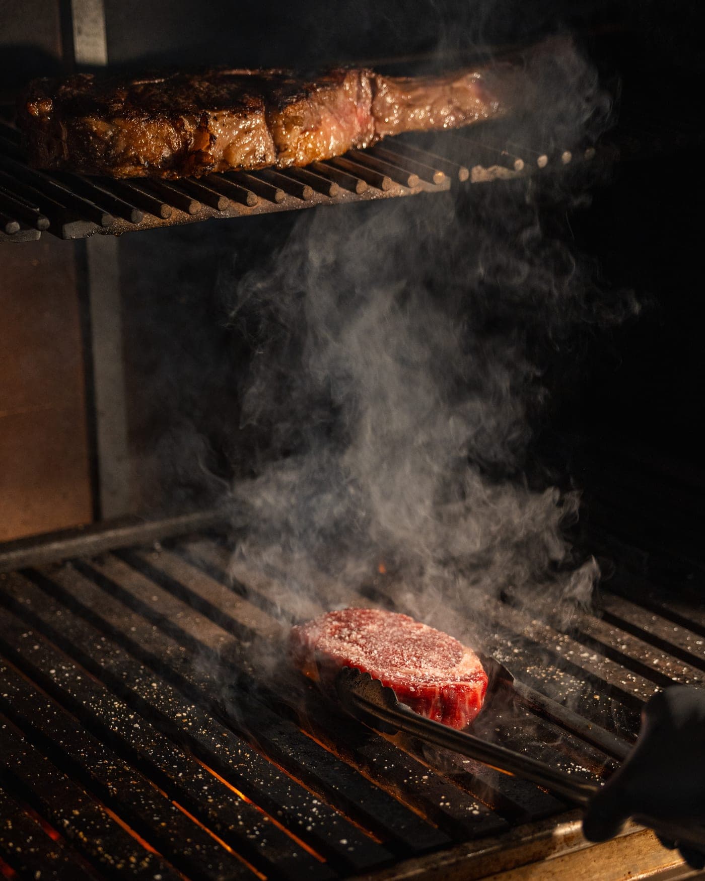 A steak searing on the grate in a plume of smoke