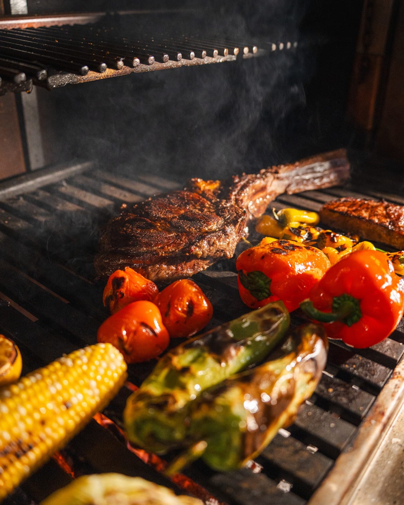 Steaks, corn and peppers side by side on the grill