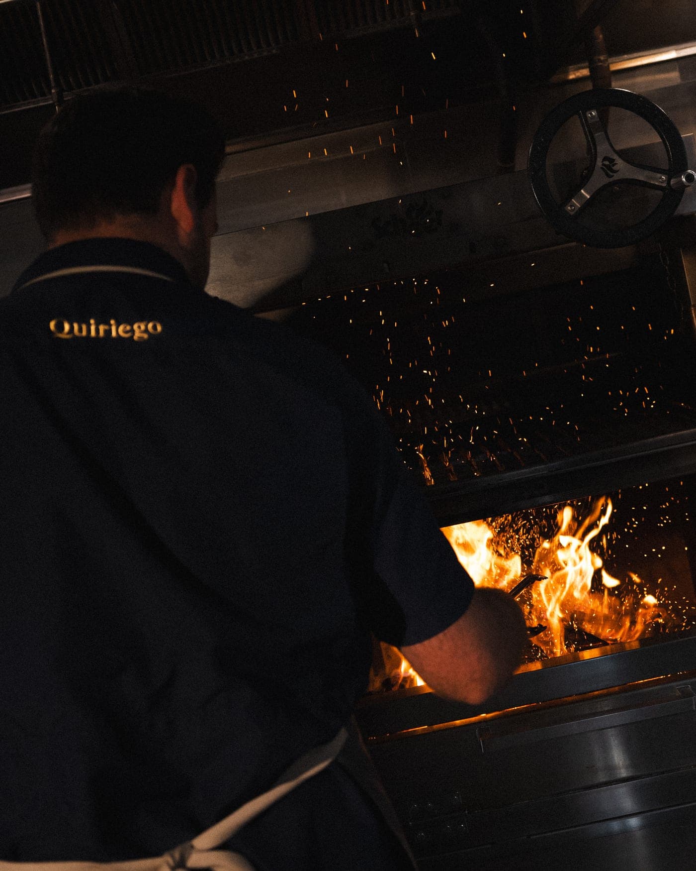 A cook tending the wood fire as sparks rise